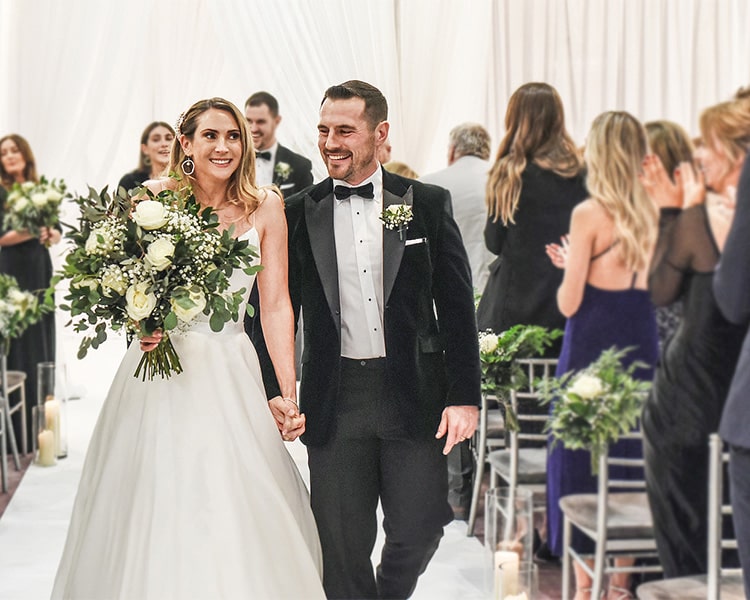 A bride and groom hold hands as they walk down the aisle of the civil ceremony at Clontarf Castle Wedding Venue in Dublin.
